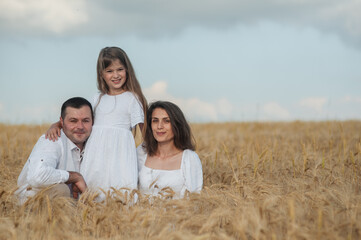 Mom, dad and  сute daughters hug in a wheat field.