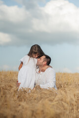 Dad and daughter hug in a wheat field.