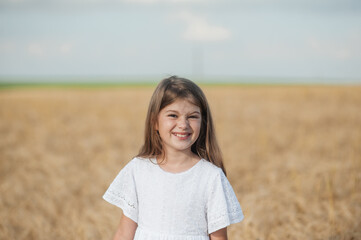 Happy child spends his childhood in the country, runs happily next to the wheat field. Child girl running through field of wheat, sunset.