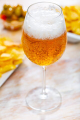 Bowl of pickled olives and portion of potato chips are laid out on plates and complement glass of allowed to cool foam frothy beer with snacks. Restaurant decoration of snacks, bar menu