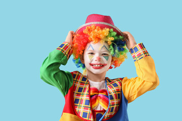 Funny little boy in clown disguise with hat on blue background. April Fool's Day celebration