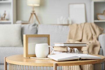 Books on coffee table with eyeglasses and cup of tea in living room. Closeup