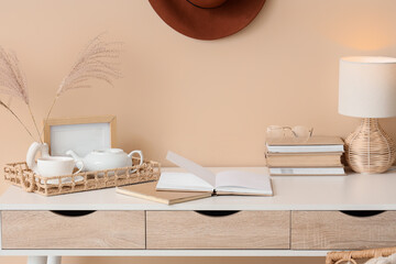 Books on workplace with teapot, cup of tea and decor near beige wall in room. Closeup