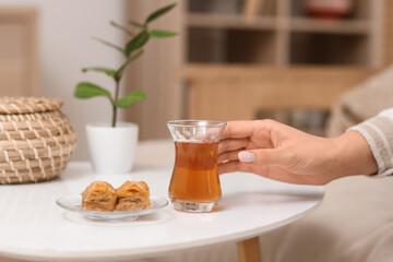Young woman taking glass of Turkish tea from table at home, closeup
