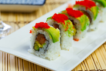 Uramaki sushi roll with salmon, mango, avocado, cucumber and tobiko served with soy sauce, wasabi and pickled ginger