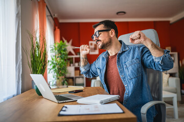 adult man stretching his arms while looking at laptop at home office