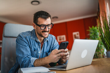 smiling man at home office use mobile phone and note book for research