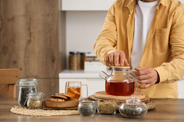 Young man with teapot, dry tea and cookies on table in kitchen, closeup