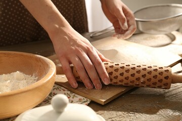 Woman with rolling pin at wooden table indoors, closeup