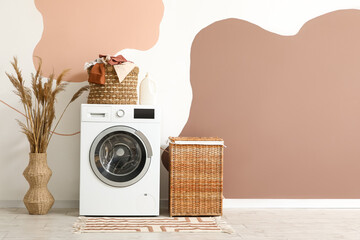 Modern washing machine with laundry baskets and pampas grass in vase near colorful wall in room