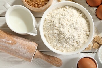 Rolling pin and ingredients for dough on white wooden table, flat lay