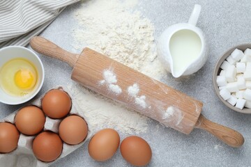 Rolling pin and ingredients for dough on light grey table, flat lay