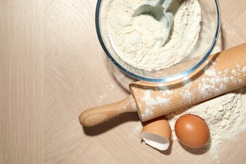 Rolling pin, flour and egg on wooden table, flat lay. Space for text