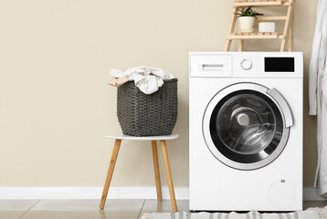 Modern washing machine with laundry basket near beige wall in bathroom