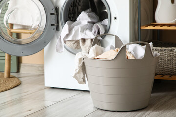 Basket with dirty clothes near washing machine in laundry room