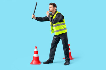 Male police officer with baton, traffic cones and whistle on blue background