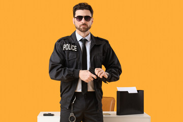 Male police officer with gun near table on yellow background