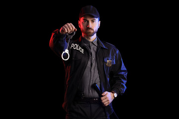 Male police officer with handcuffs and baton on black background