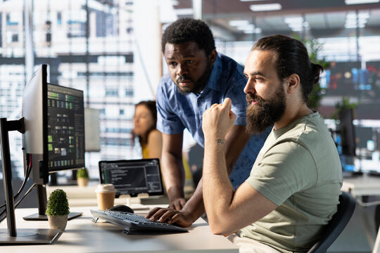 Data engineer and coworker at PC desk developing machine learning algorithms. Programmer and colleague in office solving tasks, training large scale deep learning models using computer