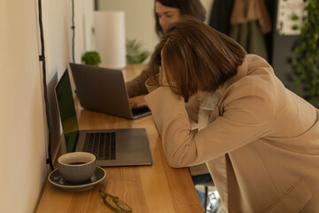 two women are working at computers in a cafe, one of them is holding her head in despair