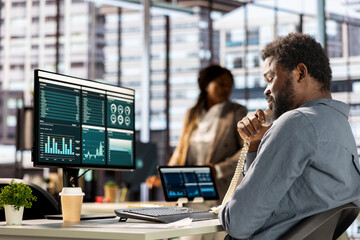 Businessman engages in a landline phone conversation at his workstation, managing a project...