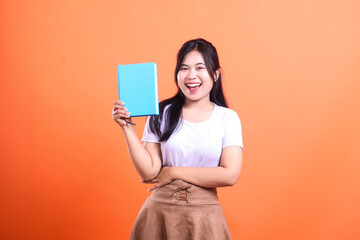 Naklejka premium A young woman with long dark hair holding a blue book in her right hand with a big smile on her face