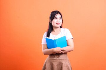 Young woman holding an open blue book while looking to the side, wearing a white t-shirt and brown skirt