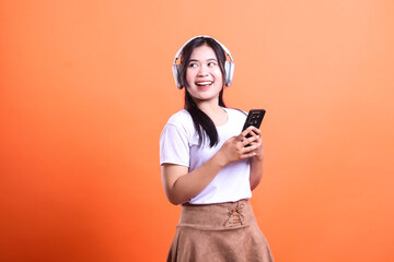 Naklejka premium Woman with Headphones Holding Phone Isolated on Orange Background while Looking Aside
