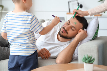 Fototapeta premium Little children painting their father's face while he sleeping at home. April fool's day prank