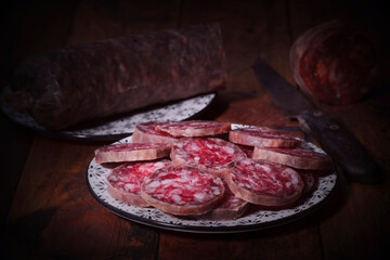 Sliced salchichon on plate with whole salami and knife on rustic wooden table