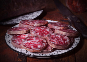 Sliced salchichon on plate with whole salami in background on rustic wooden table