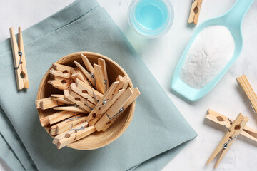 Bowl of wooden clothespins with detergent, fabric and laundry powder on white background
