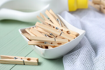 Bowl of clothespins with laundry detergent and string bag on green wooden background