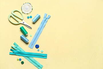 Different colorful buttons with thread spools, scissors and zippers on yellow background