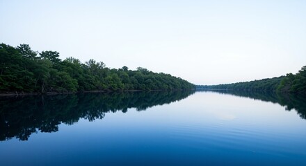 Fototapeta premium Tranquil lake reflecting lush green trees under a clear sky at dawn