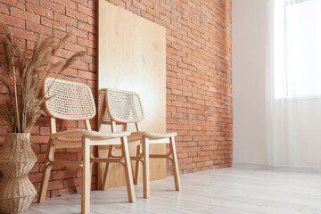 Chairs, pampas grass in vase and screen near brick wall in room