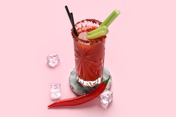 Glass of bloody mary cocktail with chili pepper, celery and ice cubes on pink background