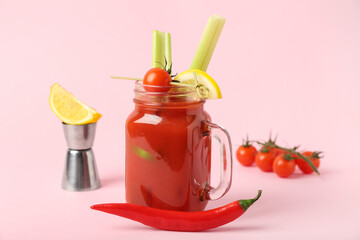 Mason jar of bloody mary cocktail with celery, chili pepper and lemon on pink background