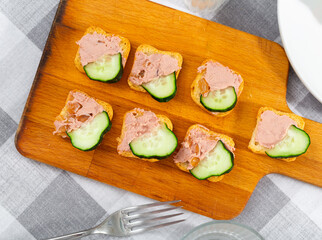 Small sandwiches with meat paste and slice of fresh cucumber are laid out and cooked on small board. Hearty homemade snack for group of friends