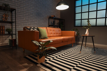 Cozy sofa, coffee table and glowing lamps in interior of modern living room in evening