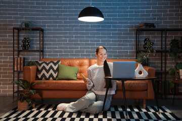 Young woman sitting on floor using laptop at home in evening
