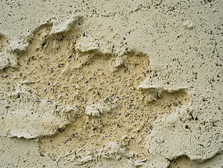 Close-up view of a damaged beige textured wall with peeling and flaking paint. Shows damage and weathering