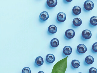 Close-up overhead shot of blueberries arranged on a light blue background with a single leaf.