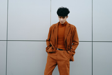 Stylish young man in brown outfit posing against a modern gray wall, exuding confidence and...