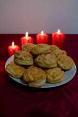Homemade golden brown cheese scones on a plate with a burgundy tablecloth, surrounded by burning red candles.