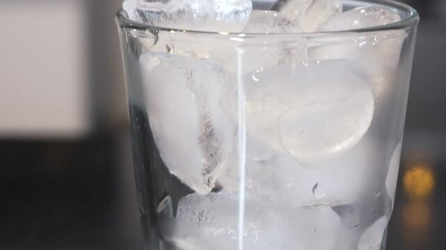 Tilt up a vaso transparente con hielo en una cocina sobre un mes&oacute;n negro.