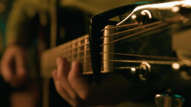 Close-up of hand of unrecognizable musician playing guitar and moving capo through finger board in dim room