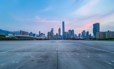 Wide angle photo of Shenzhen city skyline with empty asphalt floor, blue sky, and urban architecture at dusk.