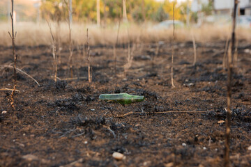 green glass bottle lies on dirty dry ground. Consequences of fire
