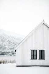 Obraz premium Nestled in a serene snowy landscape, a charming white wooden house stands against the backdrop of majestic mountains, exuding simplicity and tranquility